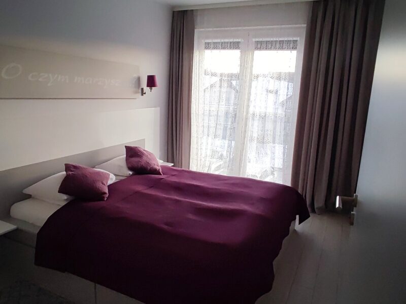 Sypialnia apartamentu Na Skarpie z fioletową pościelą i dekoracją na ścianie