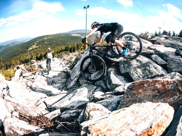Rowerzyści na skalistej trasie enduro Bike Parku Czarna Góra z panoramą Sudetów w tle